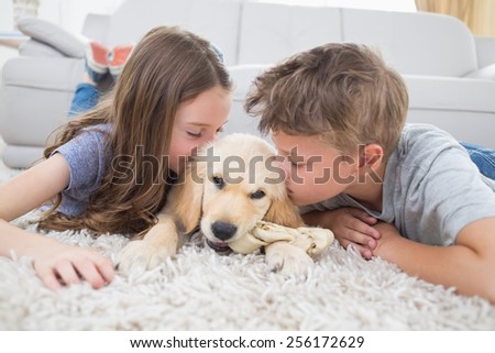 Brother and sister kissing puppy on rug at home