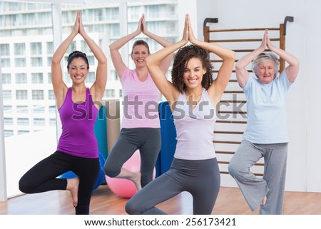 Happy female friends practicing tree pose in fitness studio