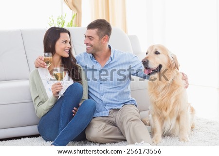 Happy couple holding wine glasses while sitting with dog at home