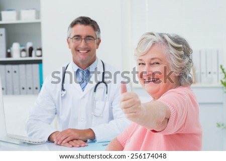Portrait of happy female patient showing thumbs up sign while sitting with doctor in clinic