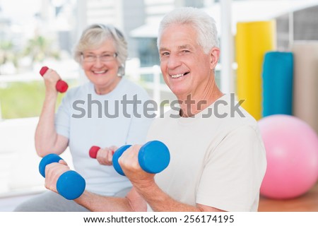 Portrait of happy senior couple lifting dumbbells in gym