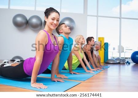 Portrait of happy woman with friends doing the cobra pose in fitness studio