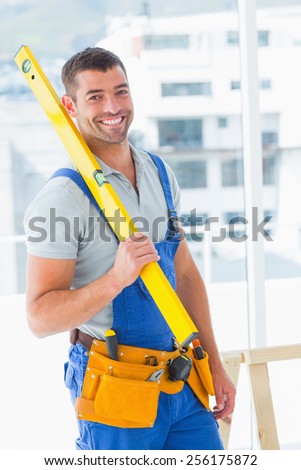 Portrait of happy repairman in overalls holding spirit level in bright office