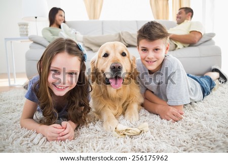 Portrait of happy siblings lying with dog while parents relaxing on sofa at home