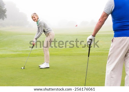 Lady golfer teeing off for the day watched by partner on a foggy day at the golf course