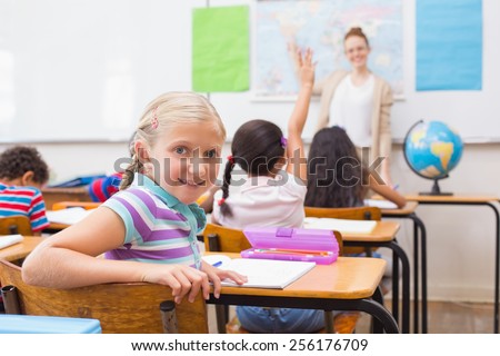 Cute pupil smiling at camera at his desk in classroom at the elementary school