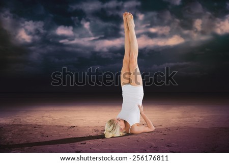 Fit young woman doing the shoulder stand pose against dark cloudy sky
