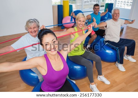 Portrait of fit people on fitness balls exercising with resistance bands in gym