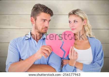 Couple holding two halves of broken heart against bleached wooden planks background