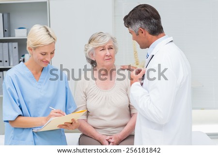 Male doctor consoling patient while nurse writing reports in clinic