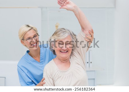 Portrait of happy senior patient being assisted by nurse in raising arm at clinic