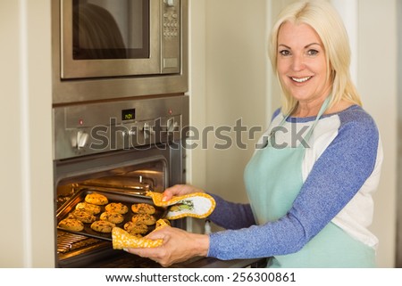 Woman taking tray of fresh cookies out of oven at home in the kitchen