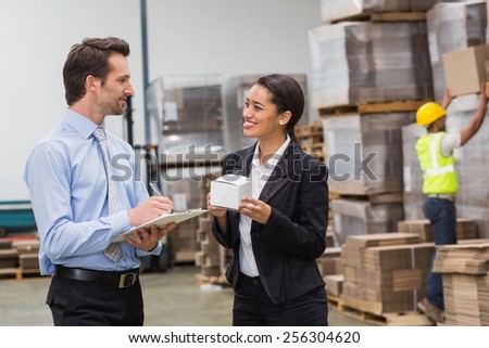 Smiling warehouse managers holding box and clipboard in a large warehouse