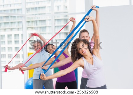 Portrait of happy female friends exercising with resistance bands in gym