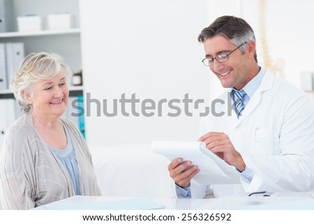Happy male doctor writing prescriptions for senior patient in clinic