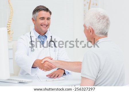Happy male doctor shaking hands with senior patient in clinc