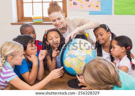 Cute pupils and teacher in classroom with globe at the elementary school