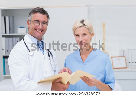Portrait of happy doctor and nurse holding report in clinic