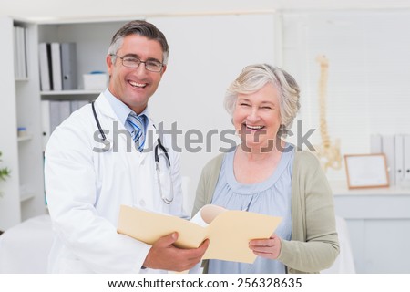 Portrait of happy male doctor and female patient with reports in clinic
