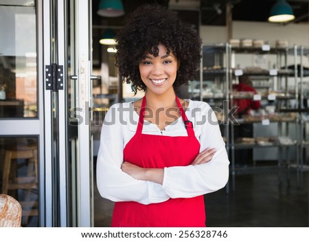 Pretty server in red apron with arms crossed at the bakery