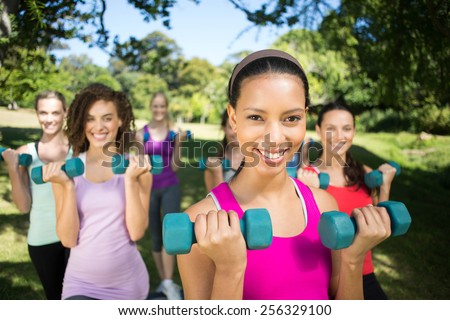 Fitness group lifting hand weights in park on a sunny day