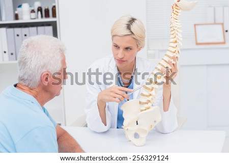 Female doctor explaning spine model to senior male patient in clinic