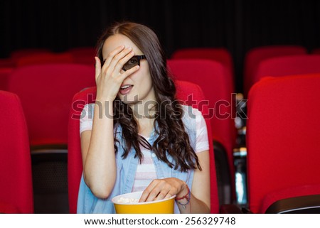 Young woman watching a scary 3d film at the cinema