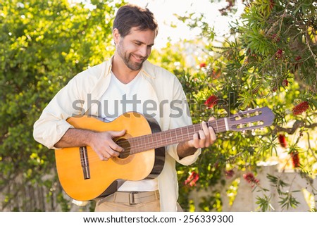 Happy man smiling at camera playing guitar on a sunny day
