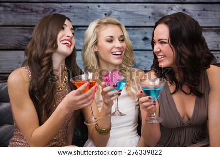 Pretty friends drinking cocktails together against grey wooden planks