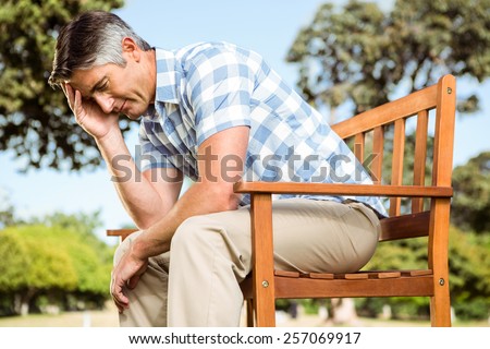 Upset man sitting on park bench on a sunny day