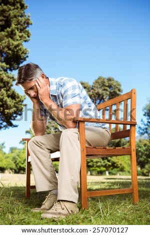 Upset man sitting on park bench on a sunny day