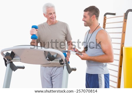Senior man on treadmill with trainer in fitness studio