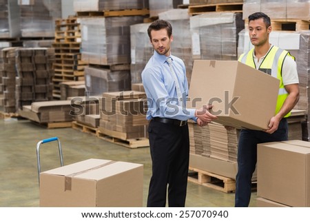 Warehouse worker and manager carrying a box together in a large warehouse