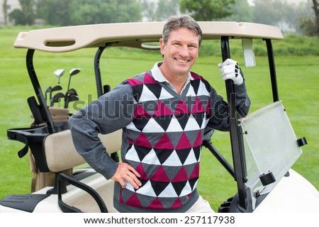 Happy golfer beside his golf buggy on a sunny day at the golf course