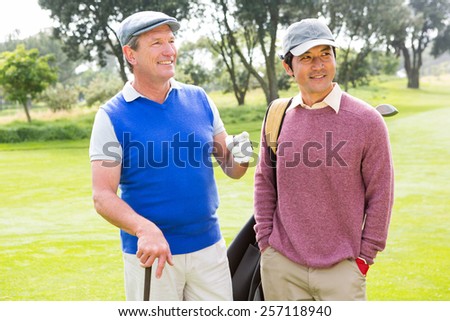 Golfing friends smiling and holding clubs at golf course