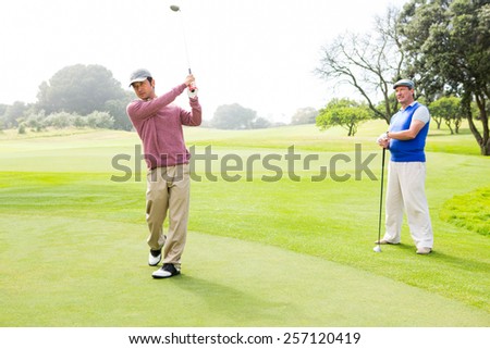 Golfer swinging his club with friend behind him at the golf course