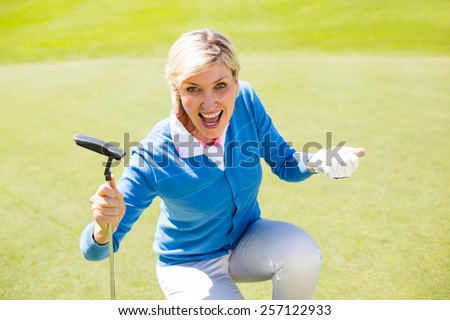 Excited lady golfer cheering on putting green on a sunny day at the golf course