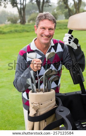 Happy golfer beside his golf buggy on a sunny day at the golf course
