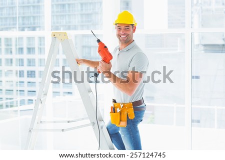 Portrait of repairman with drill machine climbing ladder in building