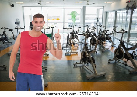 Fit man smiling and pointing against large empty fitness studio with spin bikes