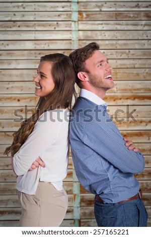 Happy young couple standing back to back against wooden background in pale wood