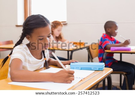 Cute pupils writing at desk in classroom at the elementary school