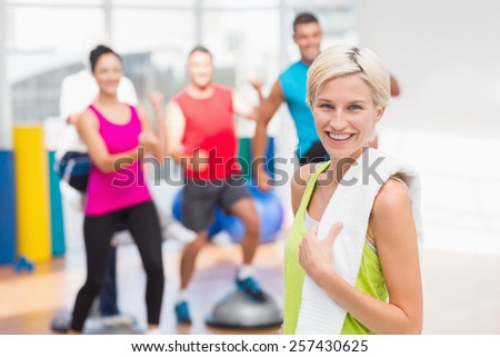 Portrait of happy woman holding towel with people exercising in background at gym