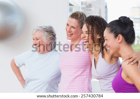 Happy female friends standing arms around in fitness studio