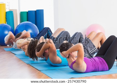 Fit men and women doing sit-ups on exercise mats at fitness club