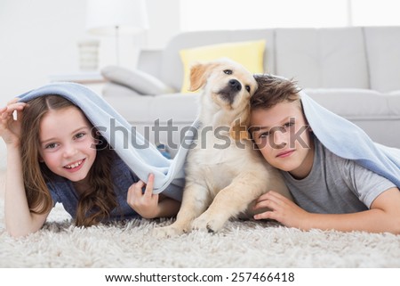 Portrait of cute siblings with dog under blanket in living room