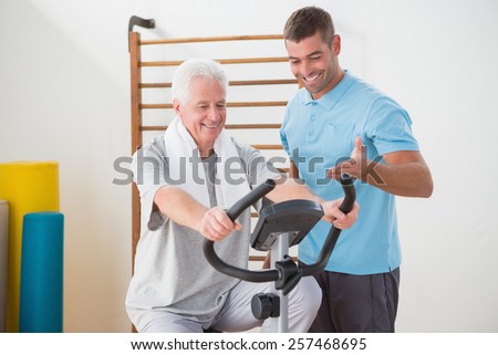 Senior man doing exercise bike with his trainer in fitness studio