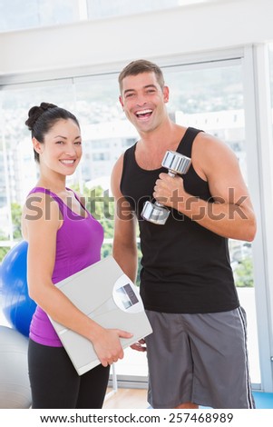 Smiling man lifting dumbbell with trainer in fitness studio