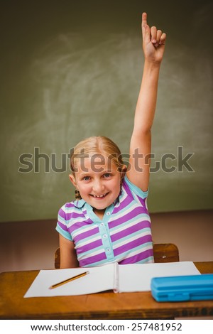 Portrait of cute little girl raising hand in classroom