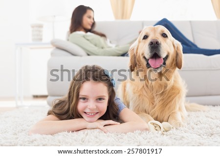 Portrait of happy girl with dog lying on rug while mother relaxing at home